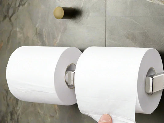 Two large rolls of white toilet paper mounted on a gray stone wall with a finger pulling a sheet