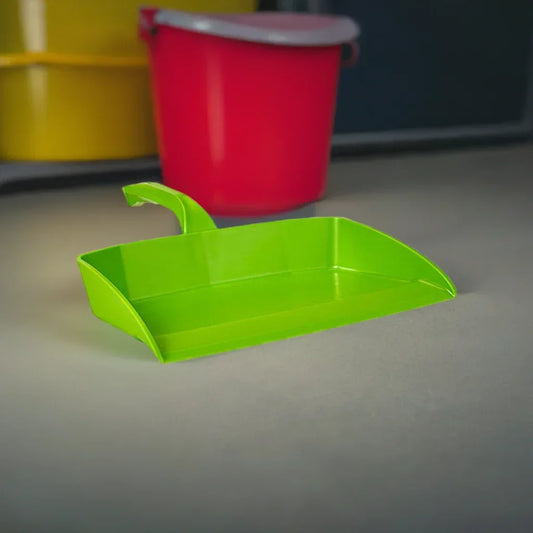 Bright green plastic dustpan with a curved handle on a gray surface, red and yellow buckets blurred in the background