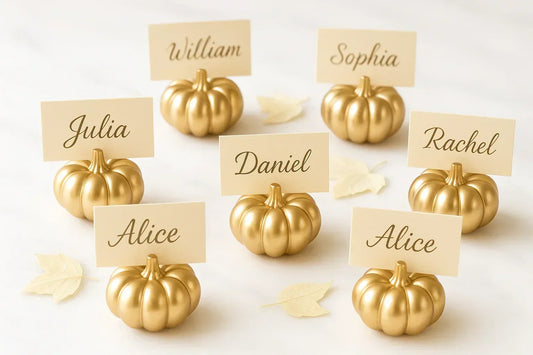 Gold pumpkin place card holders with cream name cards on a white marble surface with decorative leaves