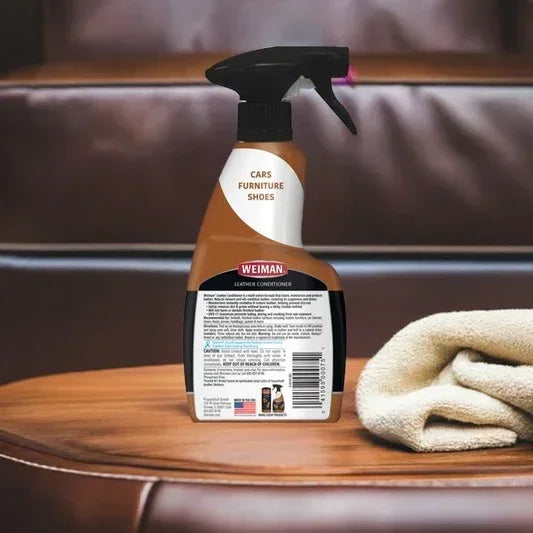 Weiman leather conditioner spray bottle for cars, furniture, and shoes on brown leather surface with folded beige cloth