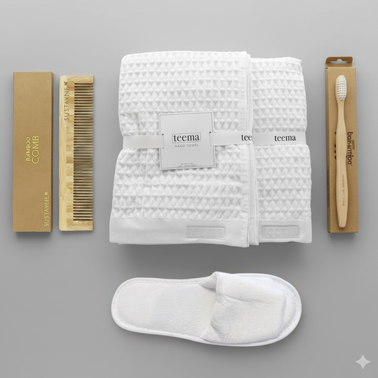 Curated luxury waffle bath towel spa gift bundle on white background, featuring a folded white organic Turkish cotton towel stack, plush velour Garnier-Thiebaut slippers, and eco-friendly bamboo essentials including a detangling comb and toothbrush.