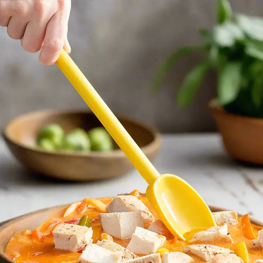 Hand holding yellow disposable spoon scooping tofu and vegetables from bowl on table