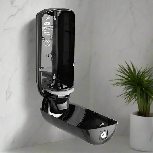 Black wall-mounted soap dispenser with open lid and lock, next to a potted green plant on marble background
