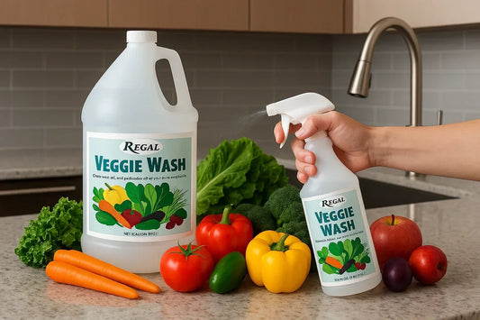 Hand spraying Regal Veggie Wash bottle near fresh vegetables including carrots, bell peppers, tomatoes, broccoli, and apples on kitchen counter