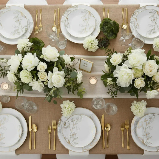 Elegant table setting with white floral patterned plates, gold cutlery, glassware, and white flower centerpieces