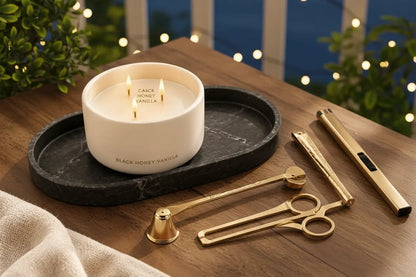Luxury candle accessory gift set with gold lighter and wick trimmer on a black resin marble tray, styled outdoors on a wooden deck veranda at dusk.