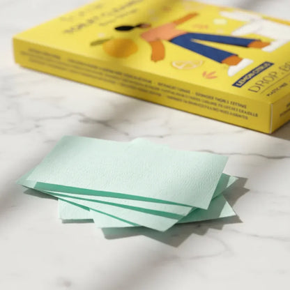 Close-up of light green toilet cleaner strips on marble surface with yellow packaging box in background