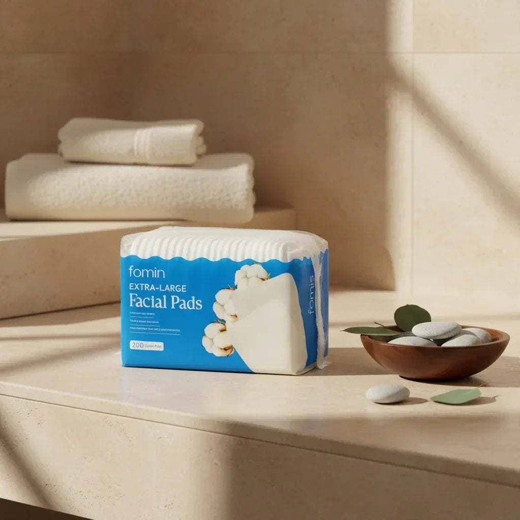 Package of fomin extra-large facial pads on beige countertop with folded towels and bowl of smooth stones