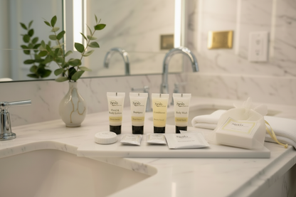 Essentials Care hotel toiletries collection by Oneuseclassic. Four white and gold tubes with soap bar arranged on a marble tray in a bright, minimalist hotel bathroom. Premium amenities for upscale guest experiences.