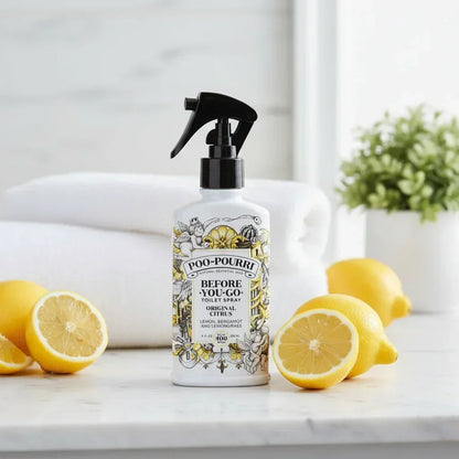 Poo-Pourri citrus toilet spray bottle with lemons, white towel, and green plant on marble surface