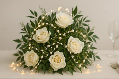 Pearl white bead string lights next to a white rose bouquet on a table