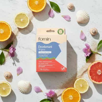 Fomin deodorant wipes variety pack box surrounded by citrus slices, flower petals, leaves, and seashells on marble surface