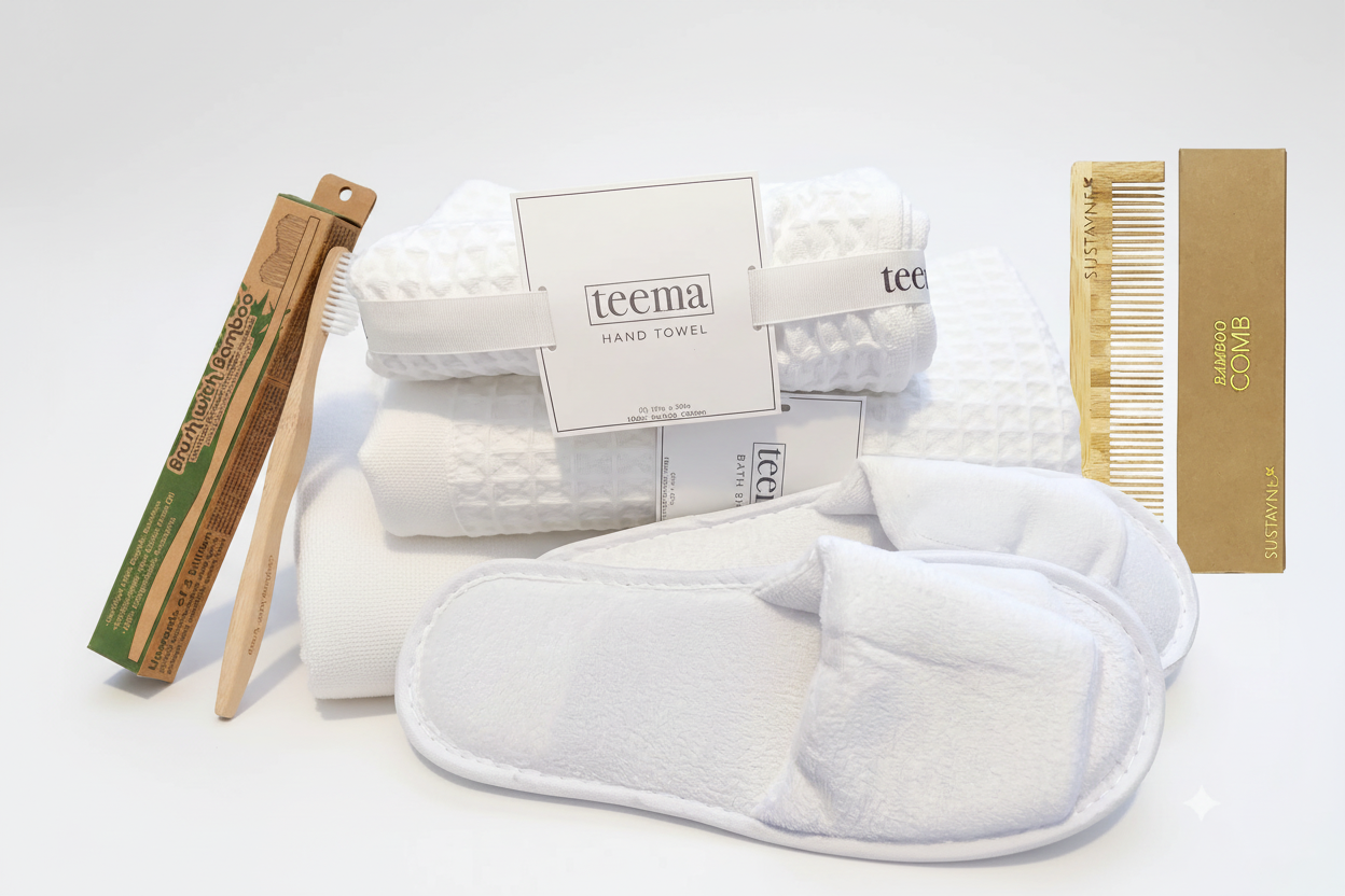 Curated luxury waffle bath towel spa gift bundle on white background, featuring a folded white organic Turkish cotton towel stack, plush velour Garnier-Thiebaut slippers, and eco-friendly bamboo essentials including a detangling comb and toothbrush.