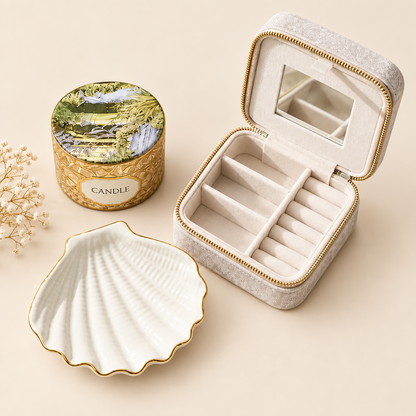 Luxury curated gift bundle containing an open champagne velvet travel jewelry case, ceramic white scallop shell dish with gold rim, and artisanal floral tin candle